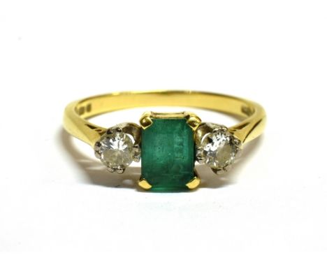 EMERALD AND DIAMOND THREE STONE DRESS RING Together with an assessment stating, central rectangular step cut Emerald measurin