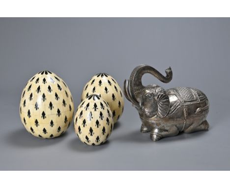 A CAMBODIAN WHITE METAL BETEL BOX IN THE FORM OF AN ELEPHANT AND A SET OF THREE INDIAN GRADUATING BONE EGG SHAPED ORNAMENTS. 