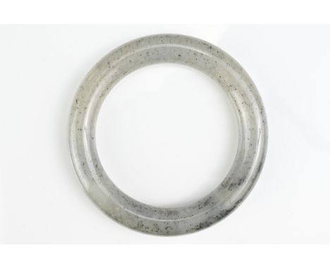 A CHINESE JADE BANGLE. Round cylindrical bangle of greyish colour with dark specs. Outer diameter 8.2cm. Inner diameter 5.6cm