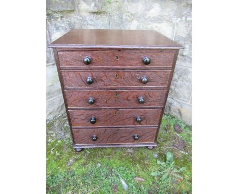A 19th century late Georgian oak miniature chest of drawers, having five graduated drawers with ebony knobs, standing on turn