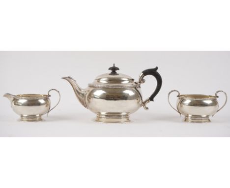 A silver three piece tea set, comprising; a teapot with black fittings, a twin handled sugar bowl and a milk jug, each piece 