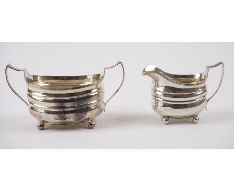 A George III silver twin handled sugar bowl, raised on four spherical feet and a George III matching silver milk jug, of helm