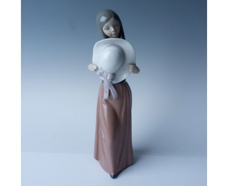 This is a Lladro porcelain figurine titled "Bashful" (No. 1005007) is an elegant piece featuring a serene young woman holding