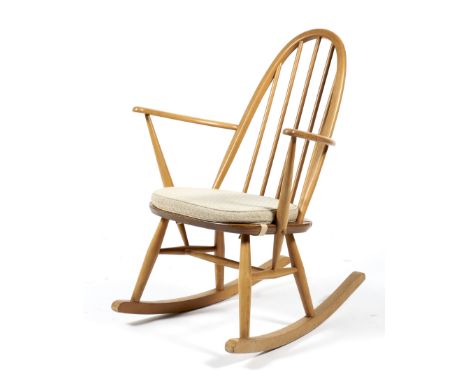 An Ercol blonde rocking chair. With arched pierced spindle back, cream cushion, blue and gilt label to reverse, H80cm 