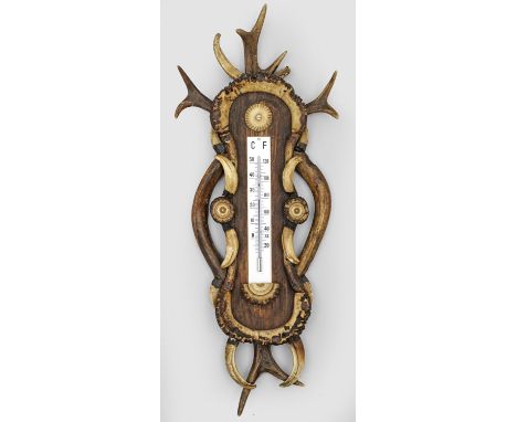 Eichenholz, dunkel gebeizt sowie Geweihteile und Wildschweinhauer. Balusterförmiger Wandschild mit Temperaturanzeige in Celsi