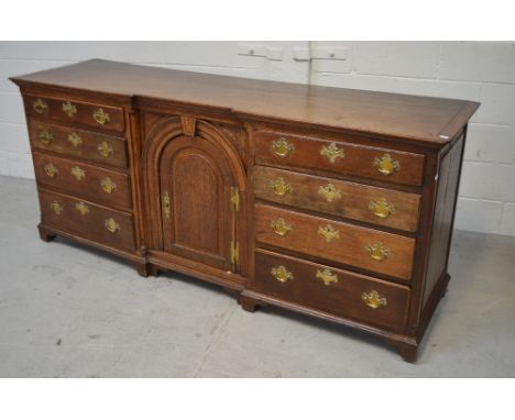 An 18th century oak sideboard, central arched door flanked either side by a row of four drawers with brass handles, overall r