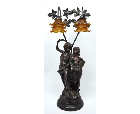 An ornate resin table lamp modelled as two scantily-clad lovers below twin amber-coloured shades, overall raised on turned eb