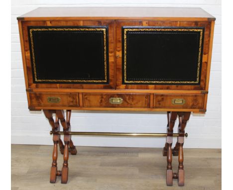 A campaign style yew wood drinks cabinet with two leather covered doors and three drawers with recessed brass handles, X-fram