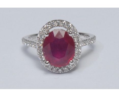 A ruby and diamond cluster ring, larger oval mid red ruby measuring approx 10.37mm x 8.76mm x 5.65mm, calculated ruby weight 