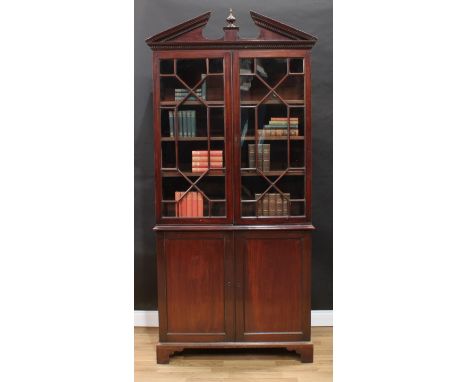 A George III mahogany library bookcase, broken-arch pediment with urnular spire finial and dentil cornice above a pair of ast