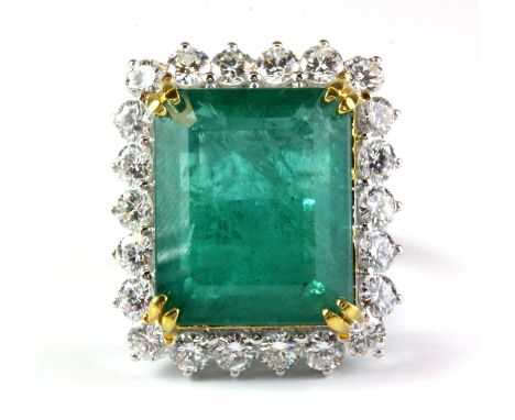 An 18ct white gold (stamped 750) ring set with a 22.37ct emerald cut natural emerald, surrounded by brilliant cut diamonds, a