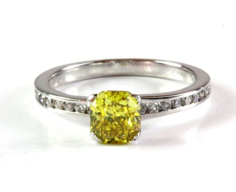 An 18ct white gold solitaire ring set with an 1.08ct cushion cut fancy vivid yellow diamond and diamond set shoulders, (M).