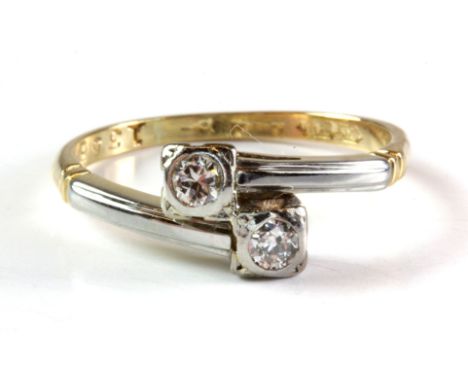 An 18ct yellow gold (worn stamp) crossover ring set with two brilliant cut diamonds, (O).