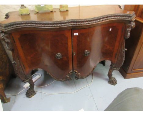 Continental walnut serpentine fronted two door commode having heavily carved decoration on cabriole paw supports, 56.5ins wid