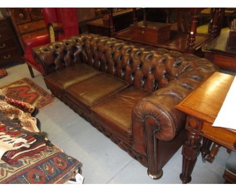 Brown leather Chesterfield three seat sofa having button upholstered back, three loose cushions and turned bun supports