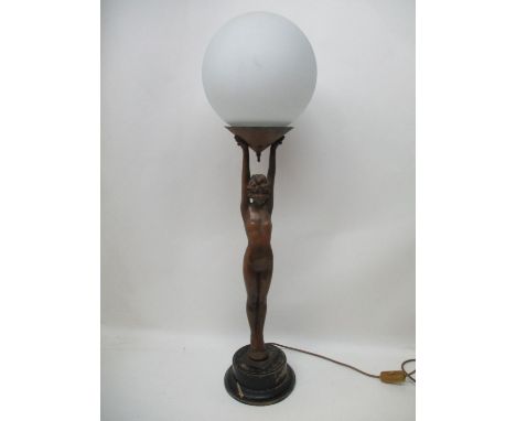 An Art Deco bronzed metal figural table lamp mounted on an ebonized pedestal base, in the form of a nude woman holding aloft 