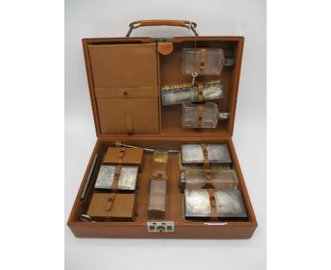 A 1940s gentleman's brown leather travelling vanity case enclosing silver lidded three glass jars, a pair of aftershave bottl