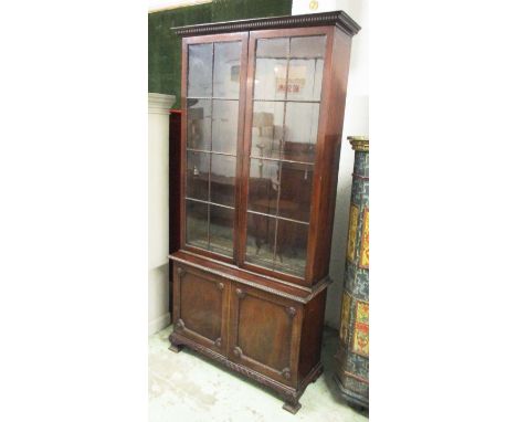 BOOKCASE, 19th century George III style mahogany with two glazed doors enclosing shelves over two panelled doors enclosing te