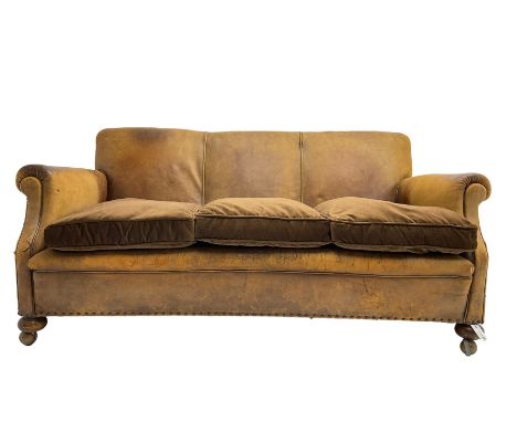 Early-to-mid-20th century three seat sofa, upholstered in worn tan leather with studwork, loose cushions upholstered in brown