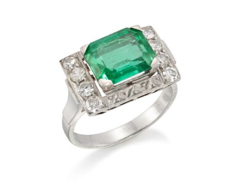 An emerald and diamond cluster ring, the central rectangular cut-cornered emerald in four-claw mount, approximate dimensions 