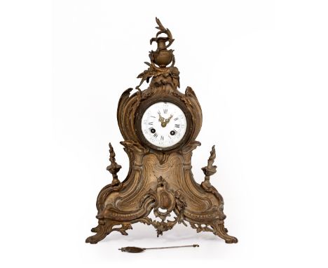 A LATE 19TH CENTURY FRENCH GILT METAL MANTLE CLOCK with an urn finial and scrolling acanthus leaf design, the enamel dial wit