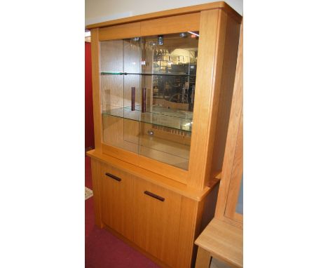 A contemporary light oak display cabinet, having twin glazed upper doors with mirrored interior, over twin cupboard lower doo