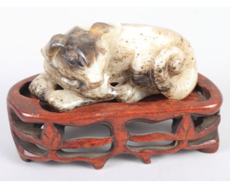 A Chinese carved jade figure of a resting dog, 3 1/4" wide, and an unmatched hardwood stand