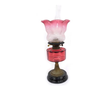 A Victorian cranberry glass oil lamp, the flared shade with etched floral detail and a cranberry glass reservoir, on brass st