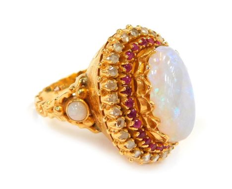 An Eastern inspired dress ring, the central oval imitation opal, in claw set, with ruby and cz set shoulders, with heavy scro