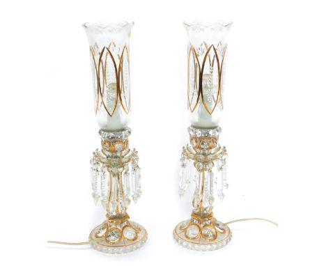 A pair of early 20thC Continental cut glass lustre table lamps, with white enamel floral decoration, gilt heightened, with br