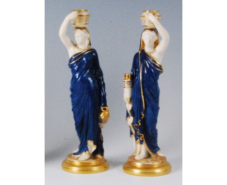 A pair of Royal Worcester figurines of water-carriers, each as robed maidens, polychrome decorated in powder blue and heighte