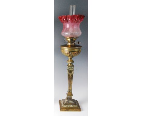 A late Victorian brass pedestal oil lamp, having cranberry tinted and acid etched shade, the brass font raised on a classical