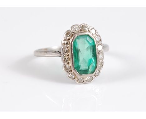 A platinum emerald and diamond ring, the rectangular octagonal step cut emerald, in rubover mount, with a surround of round s