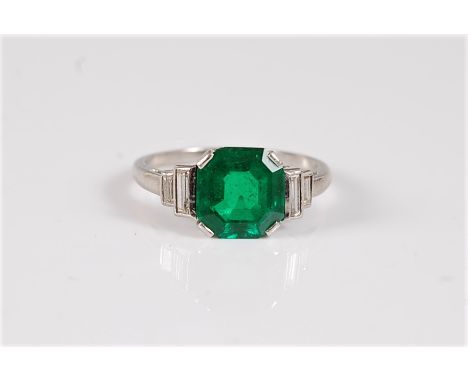 An emerald and diamond ring, the octagonal step cut emerald, approx. 8.5 x 8.1 x 4.2mm, in a four claw mount, with two baguet