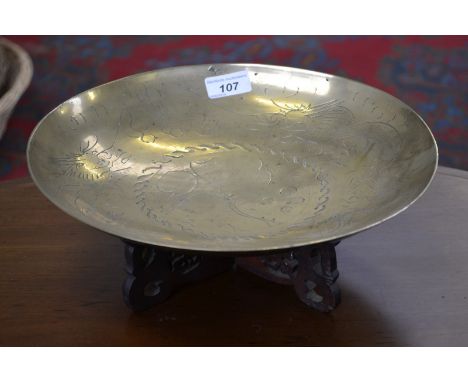 A Chinese brass dish, hand engraved with dragons chasing the flaming pearl, 30.5cm diam, pierced hardwood stand, early 20th c