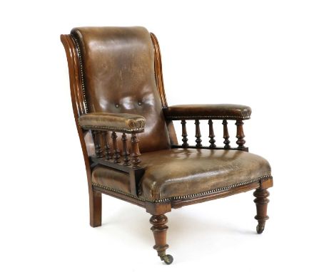 A late Victorian walnut and leather upholstered library chair,the swept back of open arms with spindle supports, raised on fr