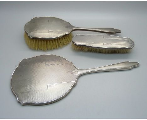 A silver backed Art Deco hand mirror, Birmingham 1944 and two matching brushes, one a/f 