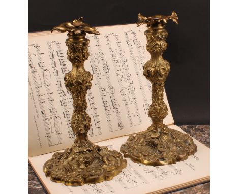A pair of French Louis XV Revival gilt bronze candlesticks, cast throughout in the Rococo taste with flowers, shells and scro