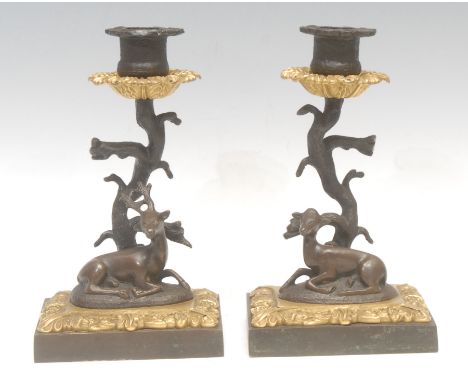 A pair of Regency parcel gilt and dark patinated bronze mantel candlesticks, each cast as a deer recumbent beside a tree, 19c