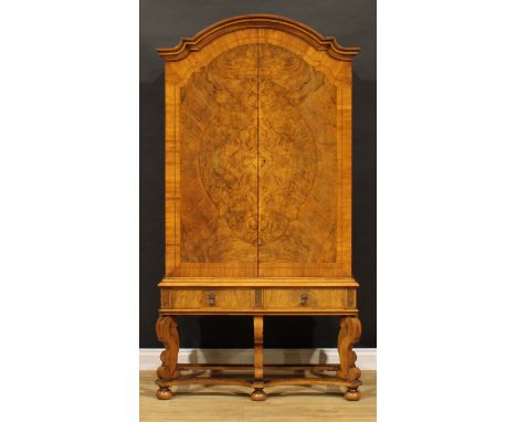 A William &amp; Mary Revival walnut cabinet on stand, shaped arch cresting above a pair of doors enclosing adjustable shelves