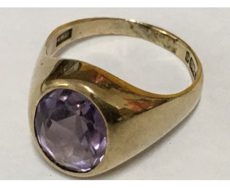 An yellow gold ring inset with an oval amethyst in rub over setting. Ring size R