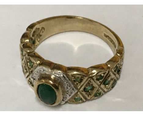 A ring inset with Cabochon emerald and diamond and emerald set shoulders in gold. Ring size M