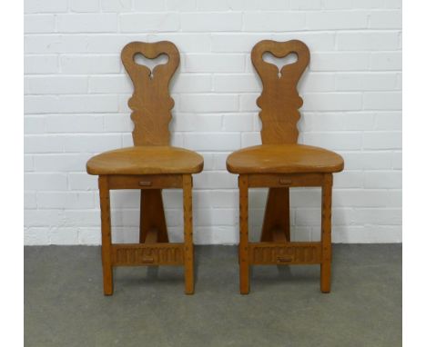 A pair of Arts &amp; Crafts style carved oak hall chairs, stylised tripod design in the manner of Rupert/Nigel Griffiths Mona
