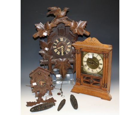 An early 20th century wooden cuckoo clock, carved crest; another similar; an early 20th century oak cased mantel clock (3)