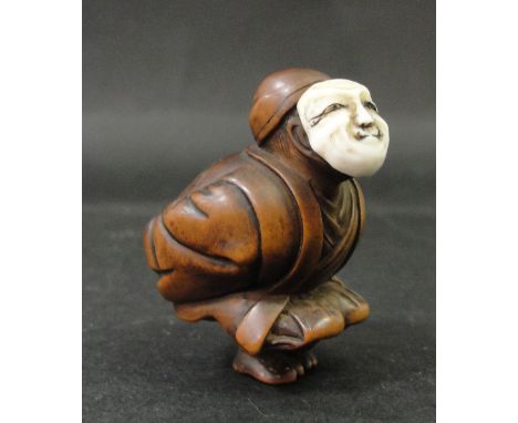 A Meiji period Ivory Faced hardwood Netsuke:
depicting a crouched man with hands behind his back wearing an ivory mask, signe