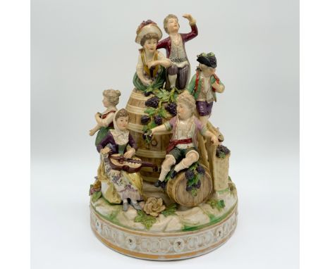 This charming figurine group, measuring 11” in height, captures a pastoral scene of six figures seated and interacting around