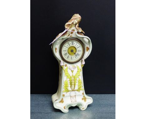 A German Art Nouveau porcelain mantle clock with female head and flowing hair to the top above the enamel dial with stylised 