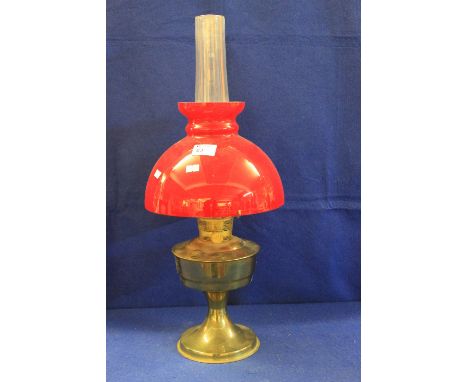 Plated metal oil lamp with circular pedestal base and red overlaid glass shade and chimney.