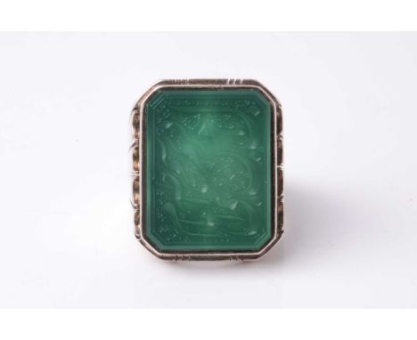 An Eastern white metal gentleman's ring set with a canted rectangular green hardstone panel intaglio cut with a probably devo