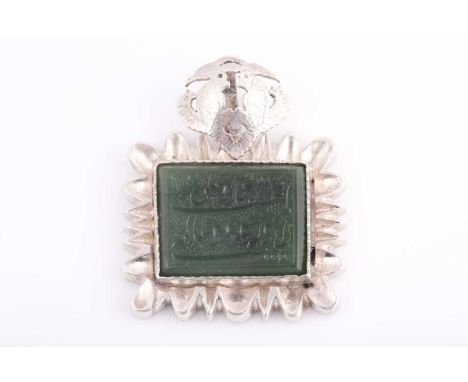 An Indo Persian white metal and jade pendant, the jaded engraved with two lines of calligraphy, within a white metal mount wi